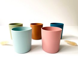 Colorful ceramic cups in various pastel shades including navy blue, old pink, light blue, ocher, and khaki. The cups have a simple, minimalist design suitable for use by babies and toddlers.