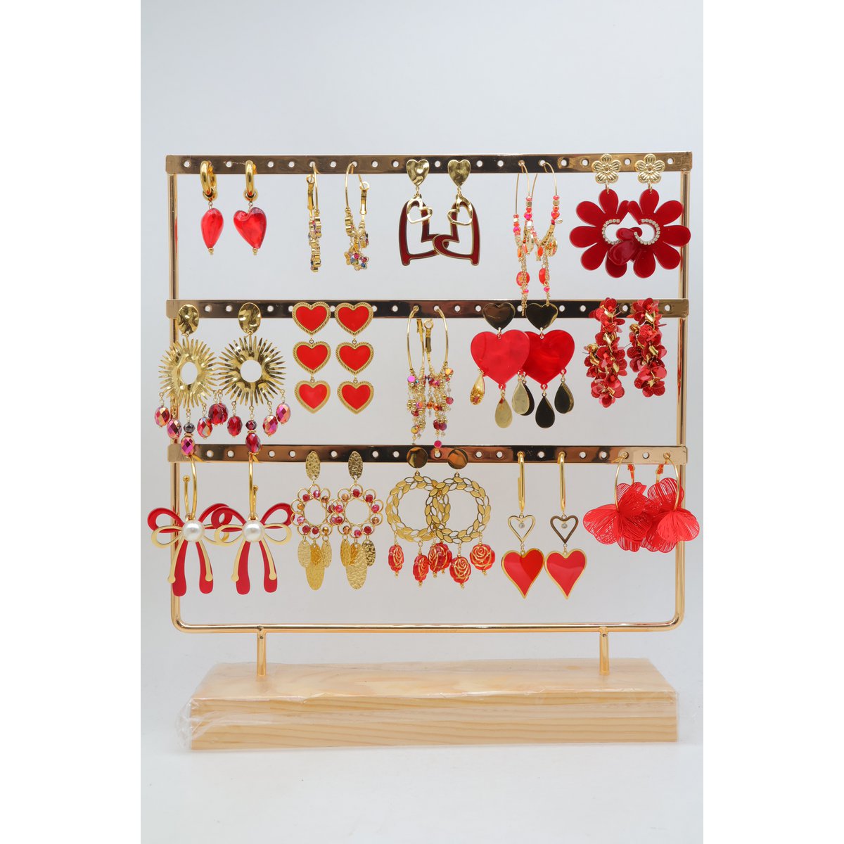 Assortiment de 15 paires de boucles d'oreilles de couleur rouge assorties, en acier inoxydable, montées sur un présentoir métallique avec un socle en bois.