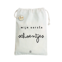 A white canvas storage bag with the text "mijn eerste schoentjes" (my first shoes) printed on it. The bag has a drawstring closure and a small circular metal charm or button attached.