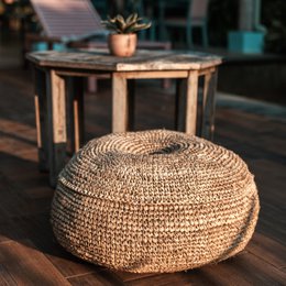 Beige round woven pouf made of raffia, available in 55 cm and 65 cm sizes, suitable for use as an ottoman or extra seating.