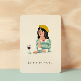 Postcard with a woman in a red beret holding a glass of wine, text reads "La vie en rose" (The life in pink).