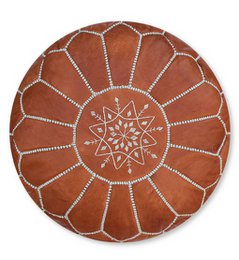 A round, brown leather pouffe with a decorative stitched pattern. The pouffe appears to be stuffed and has a textured, natural leather surface.