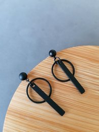 Black statement earrings with a simple, modern design featuring a circular shape and a vertical bar accent.