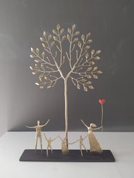 A decorative metal tree sculpture with three small human figures standing beneath it, one holding a red heart-shaped balloon.
