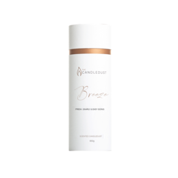 A tall, cylindrical white candle in a gift tube, with a copper-colored label. The candle is scented and part of the "Breeze" collection.