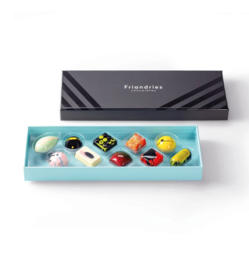 A box of assorted praline candies in various shapes and colors, including round, square, and heart-shaped pralines in shades of yellow, orange, and pink.