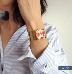 The KIMI cuff is a bangle bracelet available in various color variants including ELISE, BLANC NEIGE, RITA, OLIVIA, SARAH, and AUDE. The bracelet features a round, gold-toned design with a floral or patterned motif.