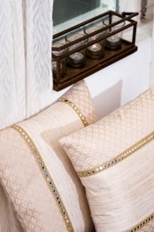 Beige handwoven cushion cover with geometric pattern and decorative border trim, natural texture.