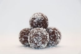 Raw cocoa energy balls in bulk, 1 kg. Spherical shape, dark brown color, coated in shredded coconut.