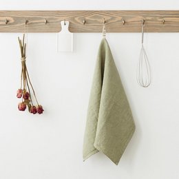 Sage green linen kitchen towel with hanging utensils and accessories.