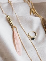Delicate golden chain necklace with a peach feather pendant and a ring with a pearl accent.