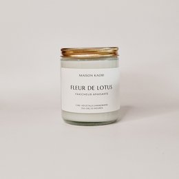 A tall, round white candle in a glass jar with a gold metal lid. The label on the jar reads "Fleur de Lotus" indicating the scent is lotus flower.