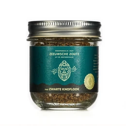 Dark green glass jar containing a spice mix with black garlic. The jar has a silver metal lid and a label with a graphic of a skull.