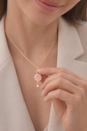 A delicate gold-tone necklace with a round pink pendant and a small dangling pearl accent.