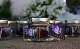 Saffron threads in a glass jar, with purple saffron flowers visible. The saffron appears to be of high quality.