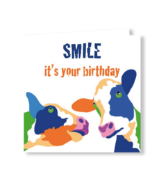 Birthday card with colorful cow, blue rabbits, orange accents, "Smile it's your birthday" text, playful festive design