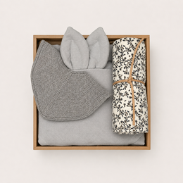 A gift box set containing soft, mellow rose-colored swaddle blankets, socks, and other accessories. The box is made of wood and includes a handwritten note.