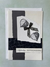 A folded condolence card with a black and white design featuring leaves and a bow. The card is suitable for expressing sympathy.