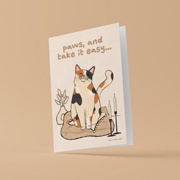 A greeting card featuring a whimsical illustration of a calico cat with the text "paws, and take it easy..."