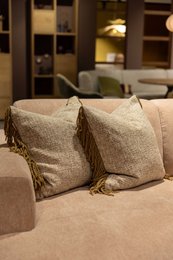 Decorative cushion with plush burgundy fabric and fringe trim, ideal for living room or bedroom decor.