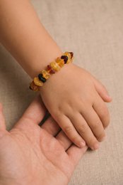 A colorful bracelet made of amber beads in various shades of yellow, orange, and brown. The beads are irregularly shaped and have a natural, raw appearance.
