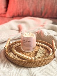  A round, tall white candle with a label that says "All you need is love" sits on a woven rattan tray, surrounded by beige and white decorative elements.