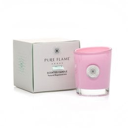 A tall, round, pink scented candle in a glass container, surrounded by white flowers. The candle is part of the "FLEUR ROYALE (PIVOINE) 'ADORE'" collection from Pure Flame.