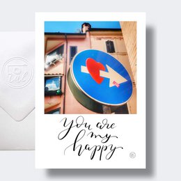 A colorful heart-shaped sign with the text "You are my happy" against a blue sky and building backdrop.