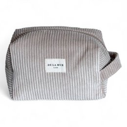 A medium-sized, beige makeup pouch with a ribbed texture and a De La Mer logo patch. The pouch has a rectangular shape and appears to be made of a soft, durable material.