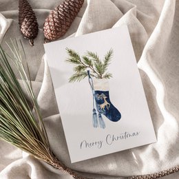 Christmas card with blue stocking, green fern, Merry Christmas text, festive holiday greeting card.