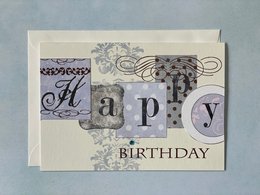 A folded birthday card with an envelope. The card features the word "Happy" in decorative text against a patterned background.