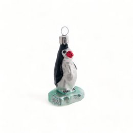 A penguin ornament standing on an ice floe, with a red beak and feet.