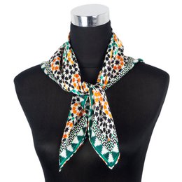 A square silk scarf with a vibrant pattern of black, orange, and turquoise stars and geometric shapes on a dark background, with a decorative border.