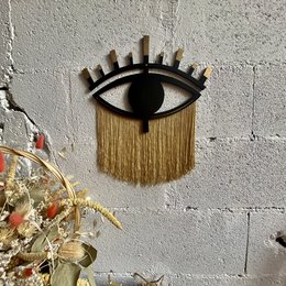 Decorative eye-shaped wall hanging made of wood and cotton thread, available in noir, pétrole, vert sapin, or, and lin color variants.