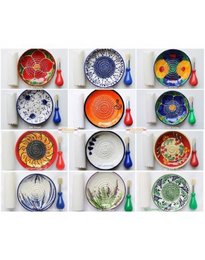 A collection of colorful ceramic graters in various patterns and designs, including round, tall, and featuring shapes like hearts, animals, and text.