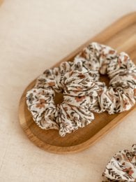 Floral patterned scrunchie made of soft, stretchy fabric in neutral tones.