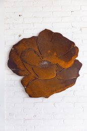 A decorative metal flower-shaped wall art piece, with a rustic, weathered appearance in shades of orange and brown.