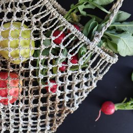  Woven basket with fresh produce, including pineapple and radishes, suspended in a macrame-style net bag.