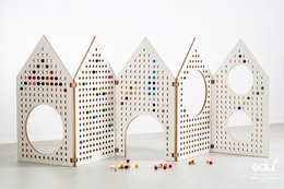 Perforated white wooden space divider with colorful beads and shapes, designed for sensory play and exploration.