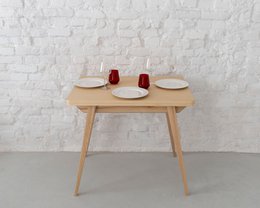 Extendable small dining table in natural ashwood with green chairs. The table can be extended and comes in various finishes including natural ashwood, oak stained ashwood, and walnut stained ashwood, with optional black legs.