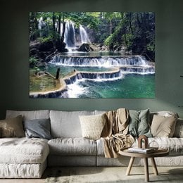 Serene waterfall in a lush, green forest setting. The image depicts a multi-tiered waterfall cascading over rocky ledges into a tranquil pool below, surrounded by dense vegetation.