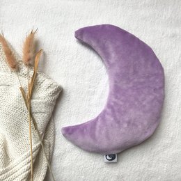 Soft, plush lilac-colored moon-shaped hot water bottle with a cozy knit cover in a neutral color palette.