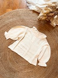 Cream-colored blouse with long sleeves and a bow detail, suitable for children aged 18 months to 6 years.