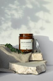 A tall, round, white scented candle with a glass jar labeled "Cotton flower". The candle is surrounded by a piece of cloth and placed on a stone surface.
