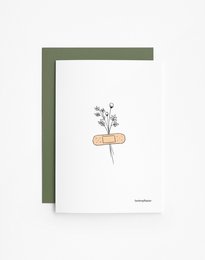 A greeting card with a simple illustration of a bandage and flowers, conveying a message of care and support.