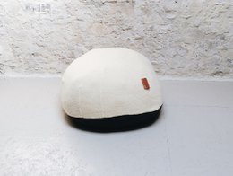 A round, white pouf with a black base. The pouf appears to be made of a soft, plush material and is designed for seating or lounging.