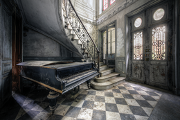 A large, ornate grand piano sits in an abandoned, dilapidated room with a checkered floor and intricate architectural details. The piano appears to be the focal point of the image.