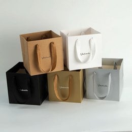 Colorful paper shopping bags in various sizes and colors, including black, silver, orange, light green, white, pink, gold, and red. The bags feature the brand name "Lanark" printed on them.