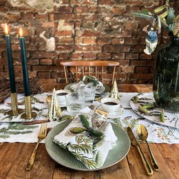 This linen table runner features a nature-inspired design with pine trees, pine cones, and other natural elements printed on a white background. It would be a beautiful and rustic addition to a dining table or other home decor.