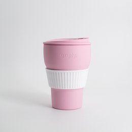 A foldable, reusable coffee cup made of silicone in a soft pink color. The cup has a textured grip and a lid for easy transport. It is a practical and eco-friendly option for enjoying coffee on the go.